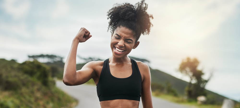 Strong mom celebrating after an outdoor workout by holding up one arm.